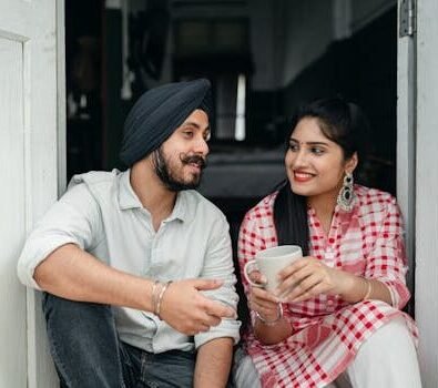 Positive Indian spouses in casual outfits sharing interesting stories while drinking morning coffee on doorstep of house